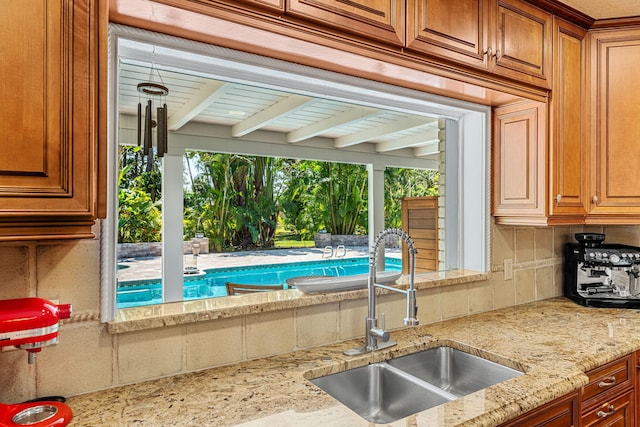 kitchen featuring beamed ceiling, sink, tasteful backsplash, and light stone counters