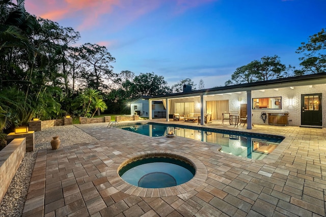 pool at dusk with a patio area and an in ground hot tub