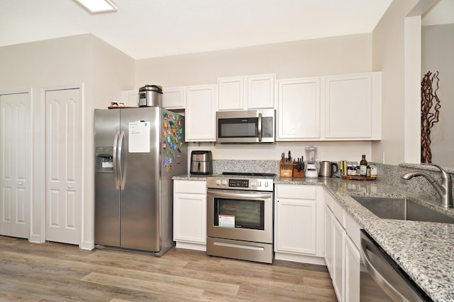 kitchen with sink, light stone counters, light wood-type flooring, stainless steel appliances, and white cabinets