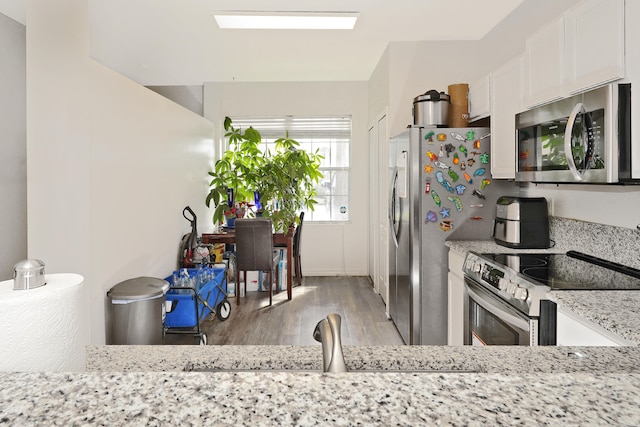 kitchen featuring light hardwood / wood-style floors, light stone counters, white cabinetry, and appliances with stainless steel finishes