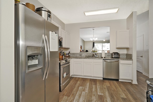 kitchen featuring wood-type flooring, appliances with stainless steel finishes, white cabinetry, and dark stone counters