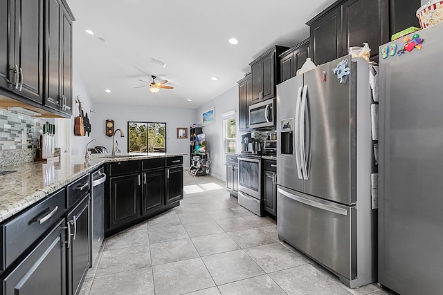 kitchen featuring backsplash, ceiling fan, appliances with stainless steel finishes, sink, and light stone counters