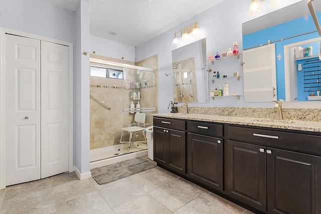 bathroom with a shower with door, dual sinks, tile flooring, oversized vanity, and a textured ceiling