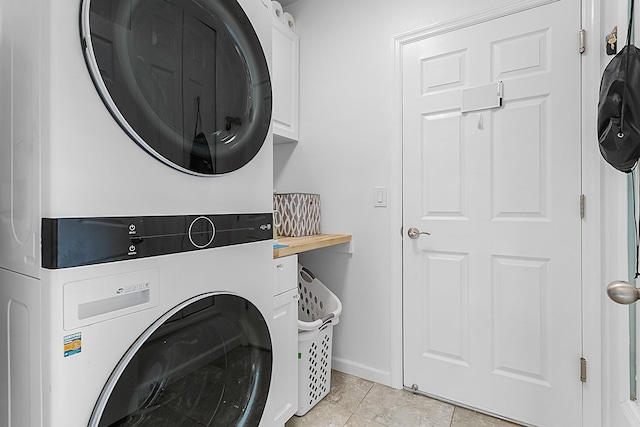 laundry area with light tile floors, cabinets, and stacked washer / drying machine