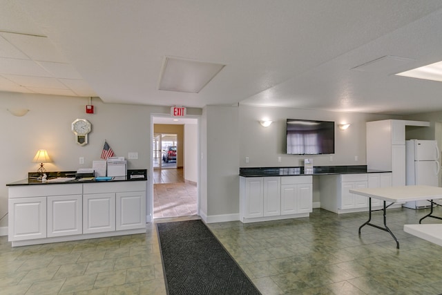 kitchen featuring light tile flooring, white refrigerator, and white cabinetry