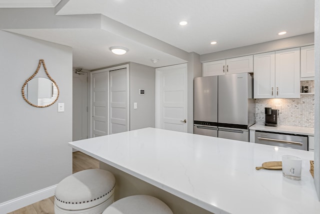 kitchen with stainless steel appliances, a breakfast bar area, white cabinets, backsplash, and light wood-type flooring