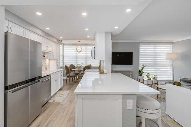 kitchen with crown molding, light hardwood / wood-style flooring, a breakfast bar area, stainless steel appliances, and white cabinetry