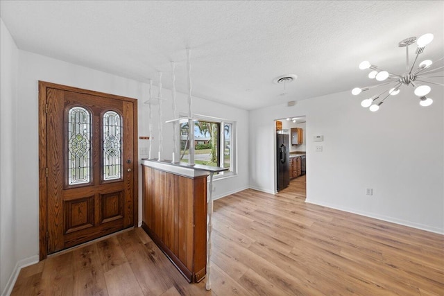 foyer entrance featuring a chandelier, a textured ceiling, and light wood-type flooring