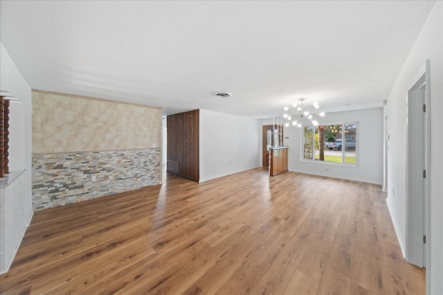 unfurnished living room with light hardwood / wood-style floors, a textured ceiling, and an inviting chandelier