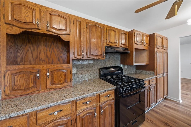 kitchen with light stone countertops, ceiling fan, light hardwood / wood-style flooring, backsplash, and black gas range