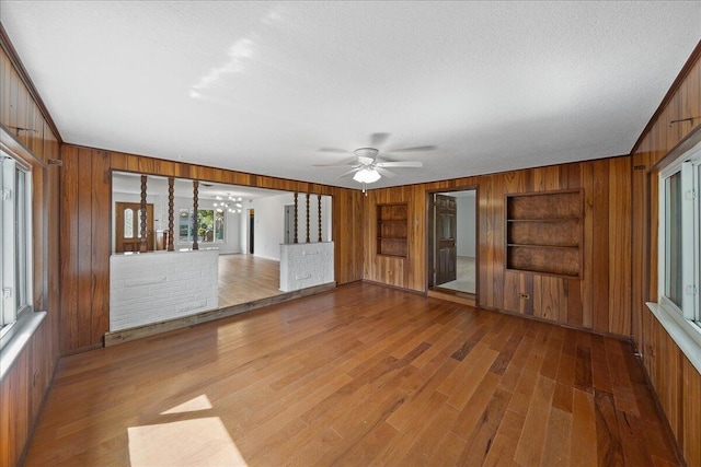 interior space with wood walls, built in features, hardwood / wood-style flooring, and ceiling fan with notable chandelier