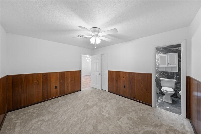 empty room featuring light carpet, a textured ceiling, ceiling fan, and tile walls