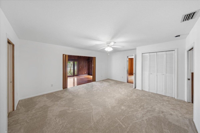 unfurnished bedroom with light carpet, ceiling fan, and a textured ceiling