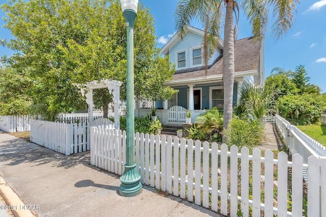 view of front of home with covered porch, a fenced front yard, a gate, and roof with shingles