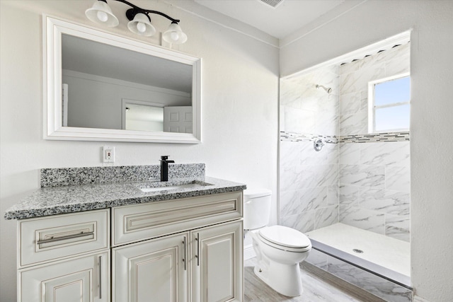 bathroom with toilet, hardwood / wood-style floors, a tile shower, and vanity