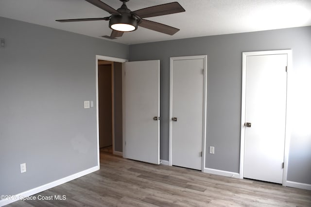 unfurnished bedroom with ceiling fan, two closets, and light wood-type flooring