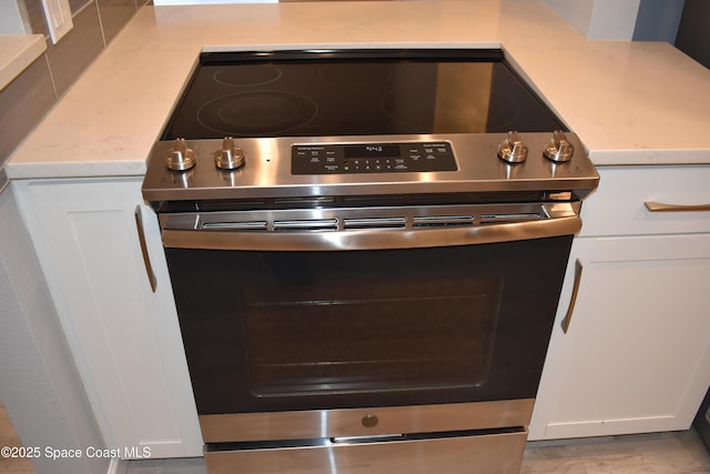 room details with white cabinetry, stainless steel electric range oven, and light hardwood / wood-style flooring