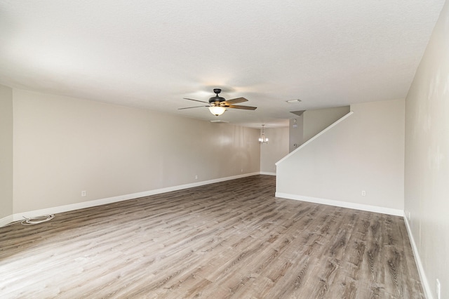 empty room with a textured ceiling, light hardwood / wood-style floors, and ceiling fan with notable chandelier