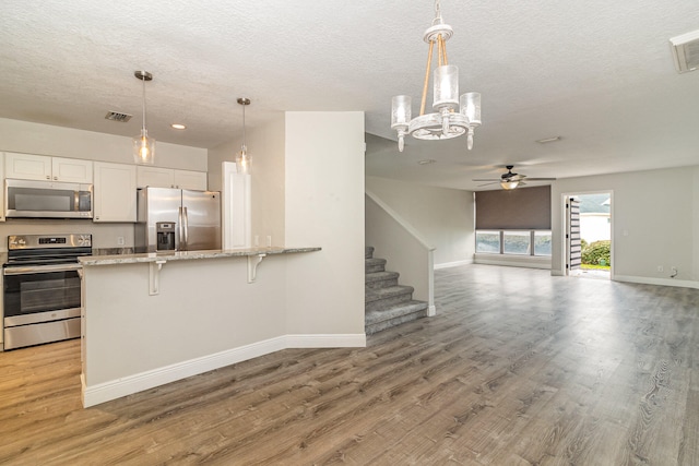 kitchen featuring white cabinetry, hanging light fixtures, light wood-type flooring, and stainless steel appliances