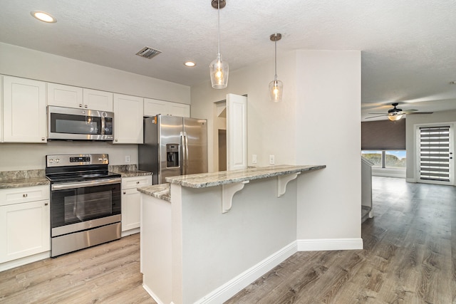 kitchen with white cabinetry, ceiling fan, appliances with stainless steel finishes, light hardwood / wood-style flooring, and pendant lighting