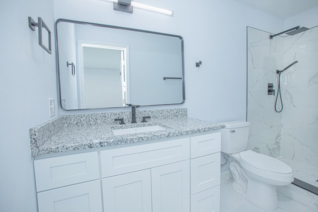 bathroom with a tile shower, vanity, and toilet