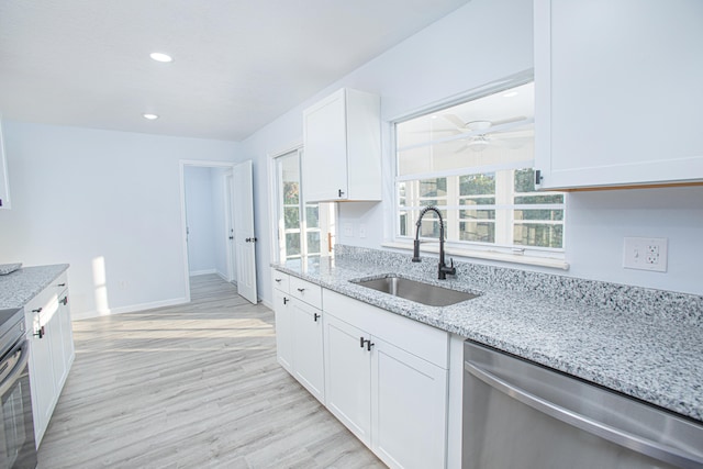 kitchen with light stone countertops, sink, stainless steel dishwasher, white cabinets, and light wood-type flooring