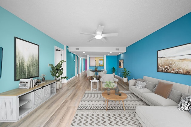 living room featuring ceiling fan, light hardwood / wood-style flooring, and a textured ceiling