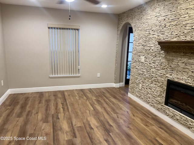 interior space featuring arched walkways, a fireplace, ceiling fan, wood finished floors, and baseboards