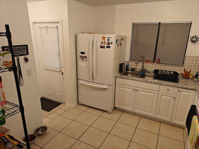 kitchen with sink, light tile floors, white cabinets, white fridge with ice dispenser, and tasteful backsplash