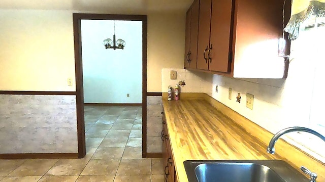 kitchen featuring wooden counters, light tile floors, an inviting chandelier, and sink