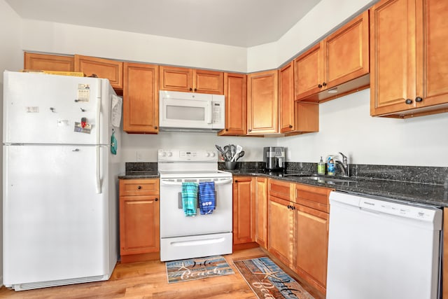 kitchen with sink, white appliances, light wood-type flooring, and dark stone countertops