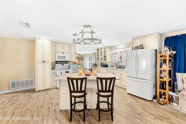 kitchen featuring a kitchen island, light hardwood / wood-style floors, white appliances, and cream cabinetry