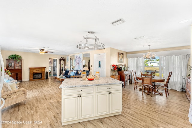 kitchen featuring light stone counters, ceiling fan with notable chandelier, light hardwood / wood-style flooring, a kitchen island, and hanging light fixtures