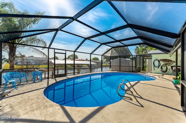 view of pool with a lanai, a water view, a patio, and a storage shed