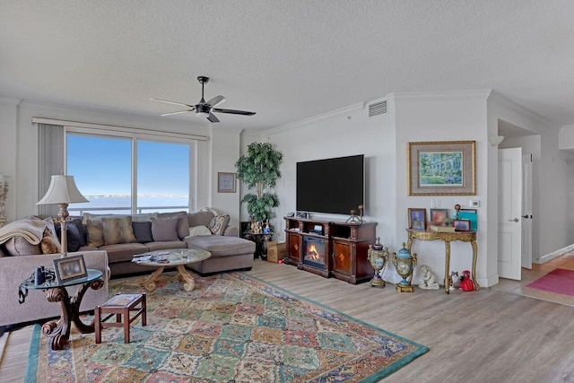 living room featuring ceiling fan, crown molding, a textured ceiling, and light hardwood / wood-style floors