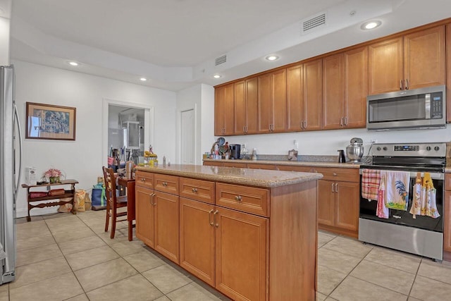 kitchen with light tile floors, light stone counters, a center island, and stainless steel appliances