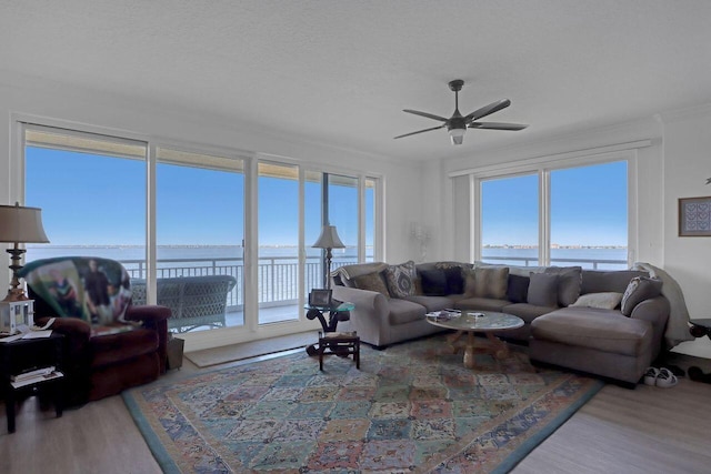 living room featuring ceiling fan, a water view, light wood-type flooring, and plenty of natural light