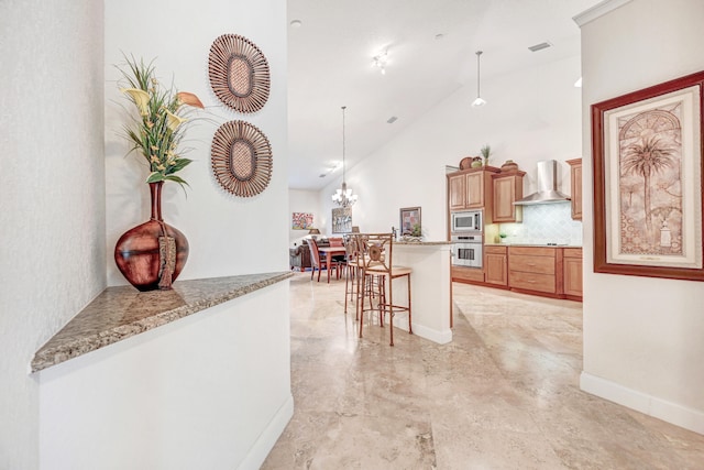 kitchen with appliances with stainless steel finishes, hanging light fixtures, backsplash, wall chimney exhaust hood, and a breakfast bar area