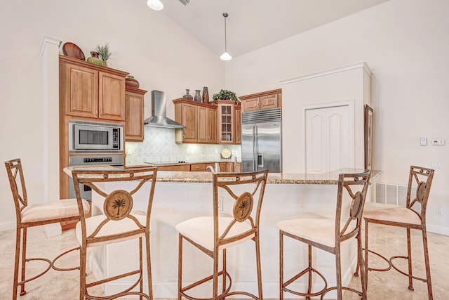 kitchen featuring backsplash, wall chimney exhaust hood, built in appliances, a center island, and decorative light fixtures