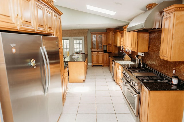 kitchen featuring light tile floors, vaulted ceiling with skylight, stainless steel fridge, dark stone counters, and double oven range