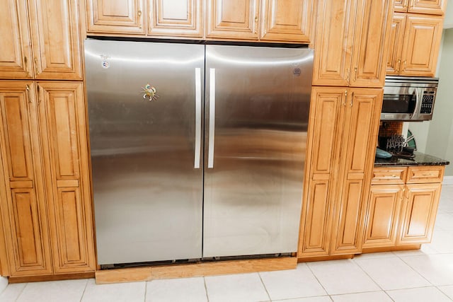 kitchen with appliances with stainless steel finishes, dark stone counters, and light tile flooring