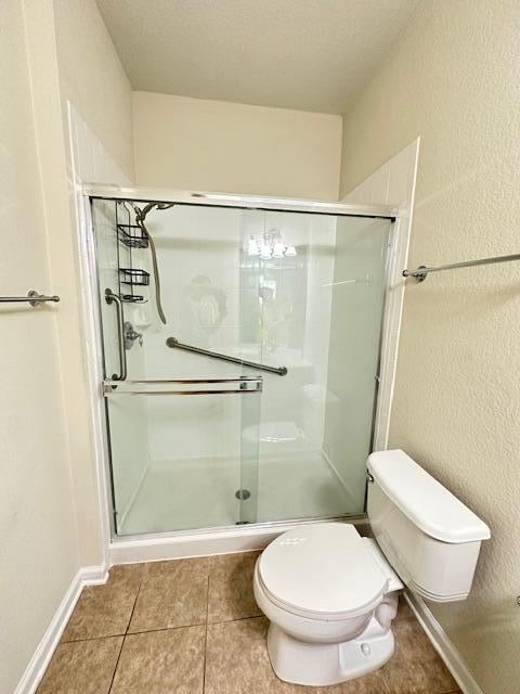 bathroom with a shower with door, tile floors, toilet, and a textured ceiling