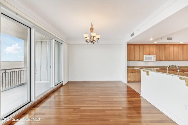 kitchen with a notable chandelier, light stone countertops, ornamental molding, and light hardwood / wood-style flooring