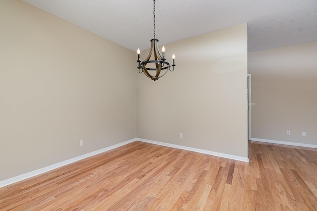 unfurnished room with light hardwood / wood-style flooring, a notable chandelier, and a textured ceiling