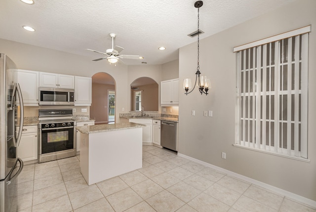 kitchen with appliances with stainless steel finishes, decorative light fixtures, white cabinets, and light tile flooring