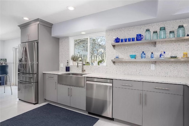 kitchen with gray cabinets, stainless steel appliances, tasteful backsplash, light stone counters, and sink