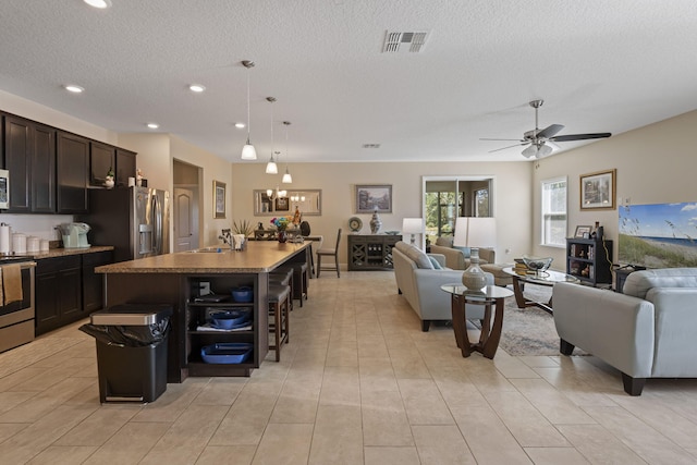 kitchen with a textured ceiling, a breakfast bar, a kitchen island with sink, and hanging light fixtures