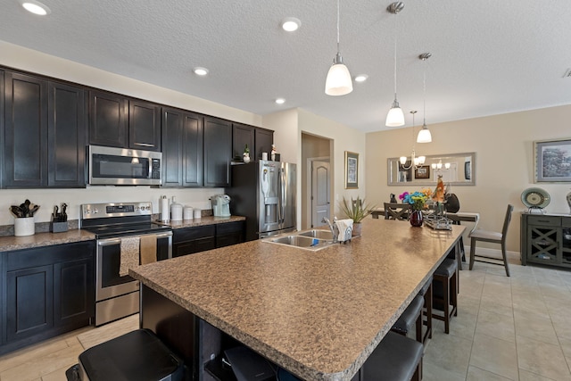 kitchen with a kitchen bar, appliances with stainless steel finishes, a kitchen island with sink, sink, and pendant lighting