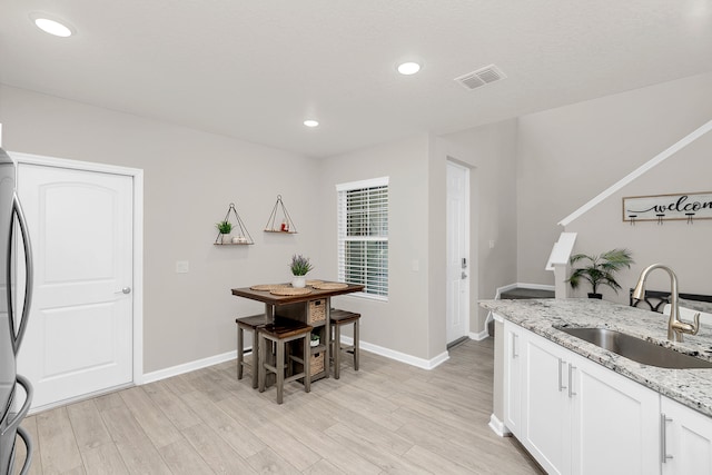 kitchen featuring white cabinets, sink, light wood-type flooring, and light stone counters