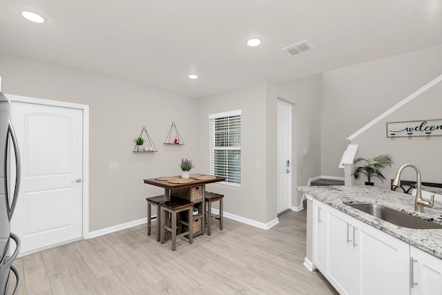 kitchen with white cabinets, sink, light hardwood / wood-style floors, and light stone counters